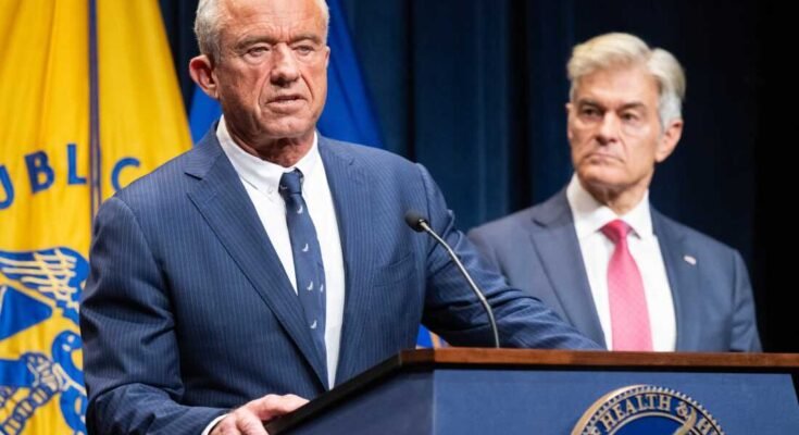 Az Egészségügyi és Szociális Szolgáltatások titkára, Robert F. Kennedy Jr. hétfőn újságíróknak szól, míg a Medicare és a Medicaid adminisztrátora, Dr. Mehmet Oz (R) hallgat. A két férfit egy dobogó mögött látják, amelyen a HHS logója van rajta.