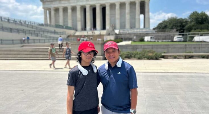 Jeffrey Pagulong (jobbra) és az ő 12 éves fia, Christof a Lincoln Memorial közelében, Washington DC -ben tartják, mindkettő piros baseball sapkát és fehér nyakhűtés -ventilátort visel.